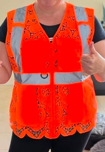 A woman giving a thumbs up in the Tangerine Orange multi-pocket vest: two flapped chest pockets, a D-ring, reflective bands, and a scalloped lace hem.